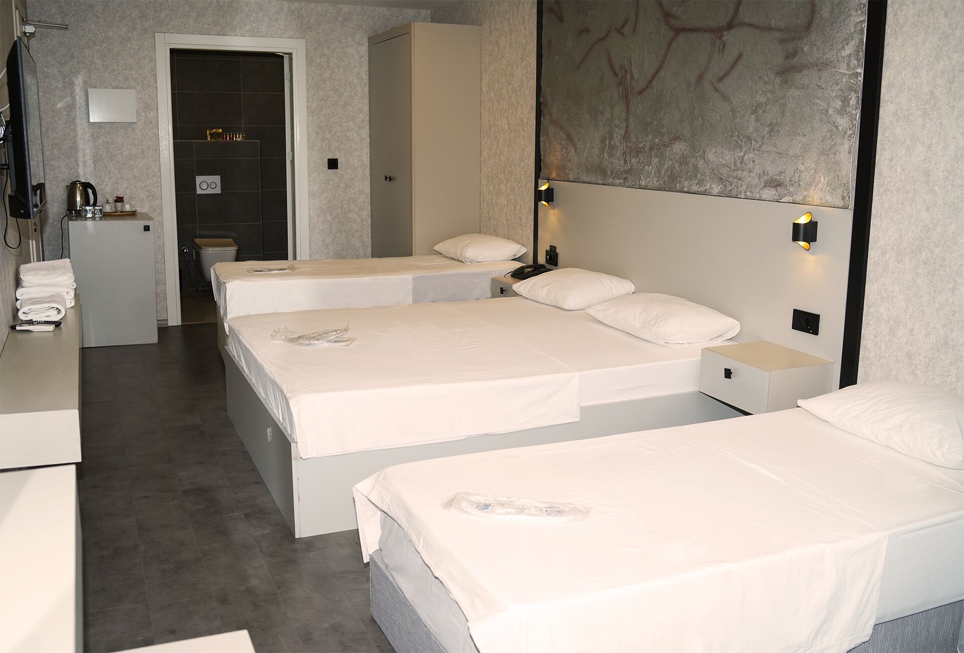 Habitación de hotel con tres camas individuales, un pequeño kitchenette y un baño.