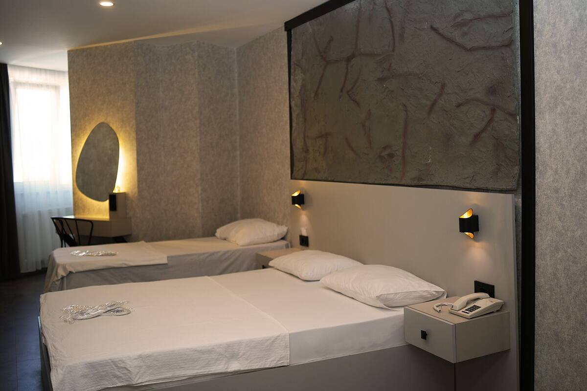 Ett hotellrum med två separata sängar, ett litet skrivbord och ett nattduksbord med en telefon.