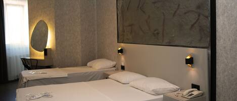 A hotel room with two single beds, a small desk, and a nightstand with a phone.