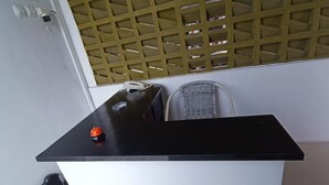 A small kitchenette with a black countertop, a white base, a wicker chair, and a door with a wooden lattice. - Hotel O Bumi Tenang Homestay (Salatiga)