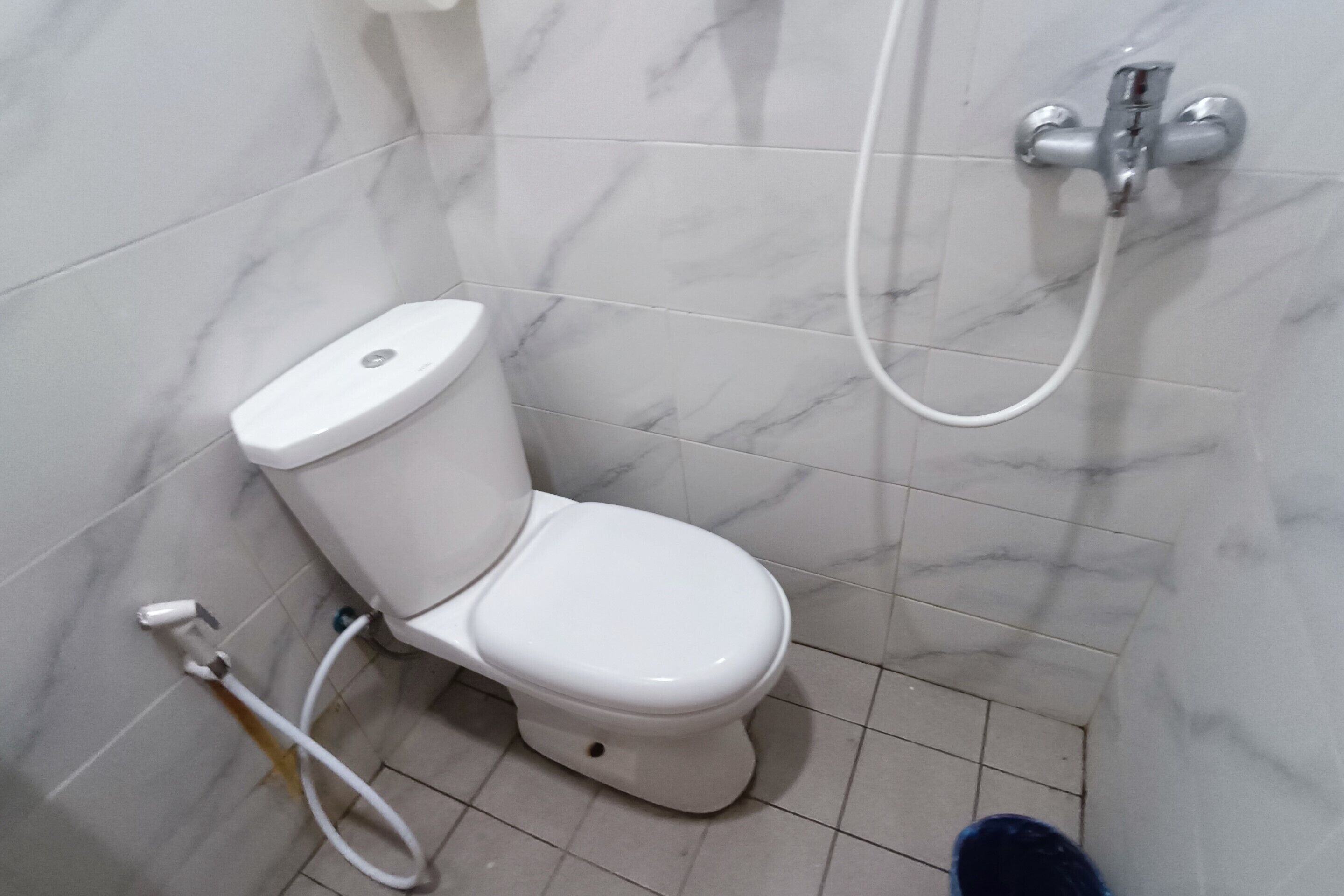 Un baño con inodoro, ducha y pared con azulejos de mármol.
