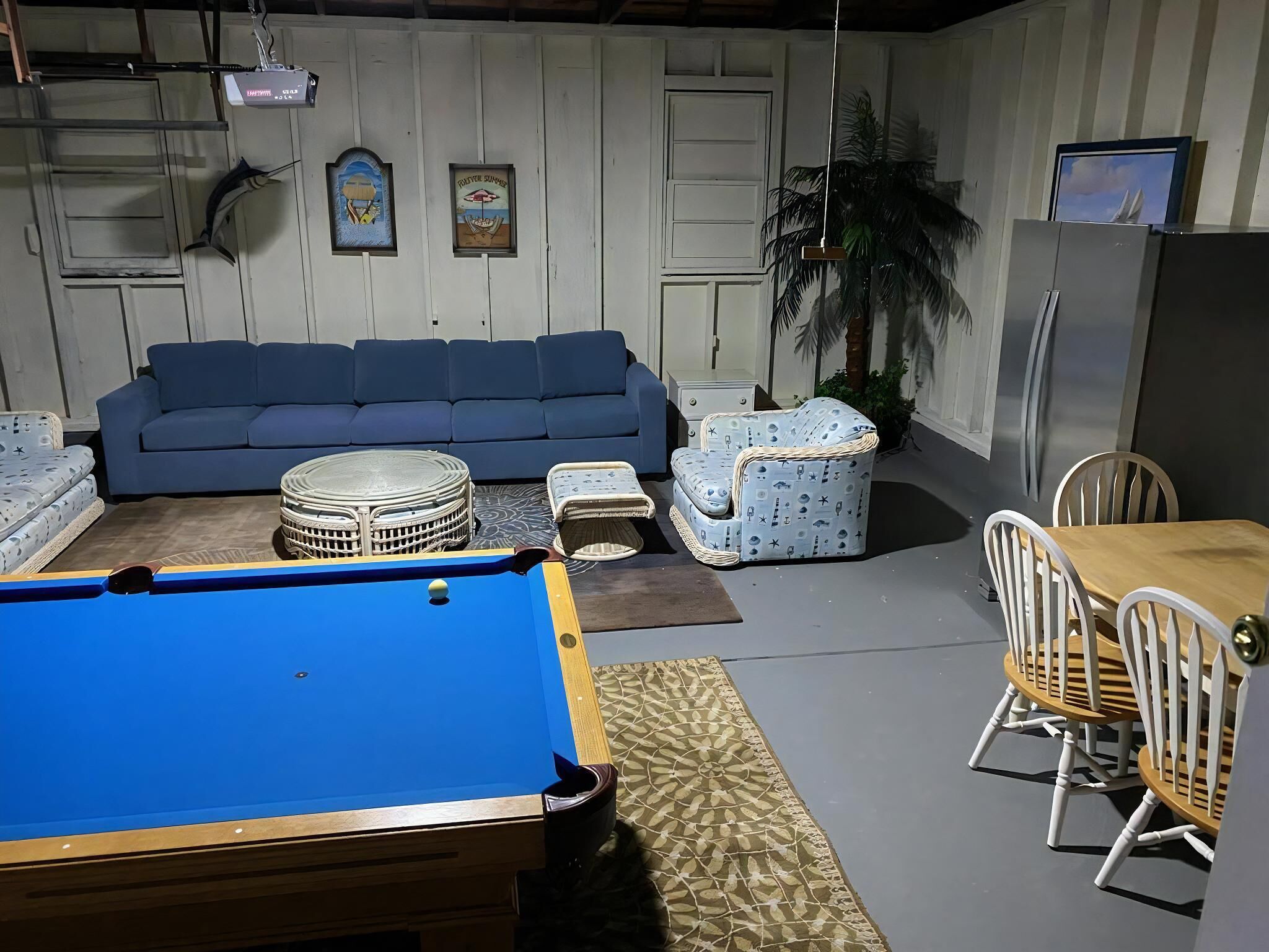 Une pièce avec une table de billard, un canapé bleu, des fauteuils à motifs et une table à manger avec des chaises.