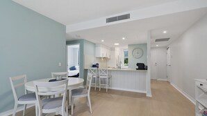 A modern kitchen with white cabinets, a central island, and a dining area with white chairs. - Blissful Bribie Beach Haven (WOORIM)