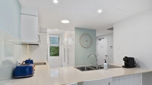 A modern kitchen with a central island, a sink, and a clock on the wall. - Blissful Bribie Beach Haven (WOORIM)