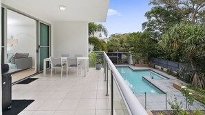 A modern apartment with a balcony, a pool, and a view of lush greenery. - Blissful Bribie Beach Haven (WOORIM)