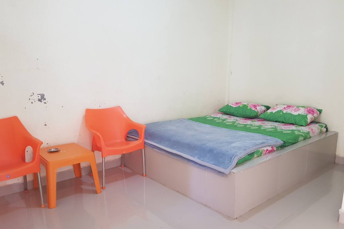 A small, simple room with a bed, two orange chairs, and a small table.