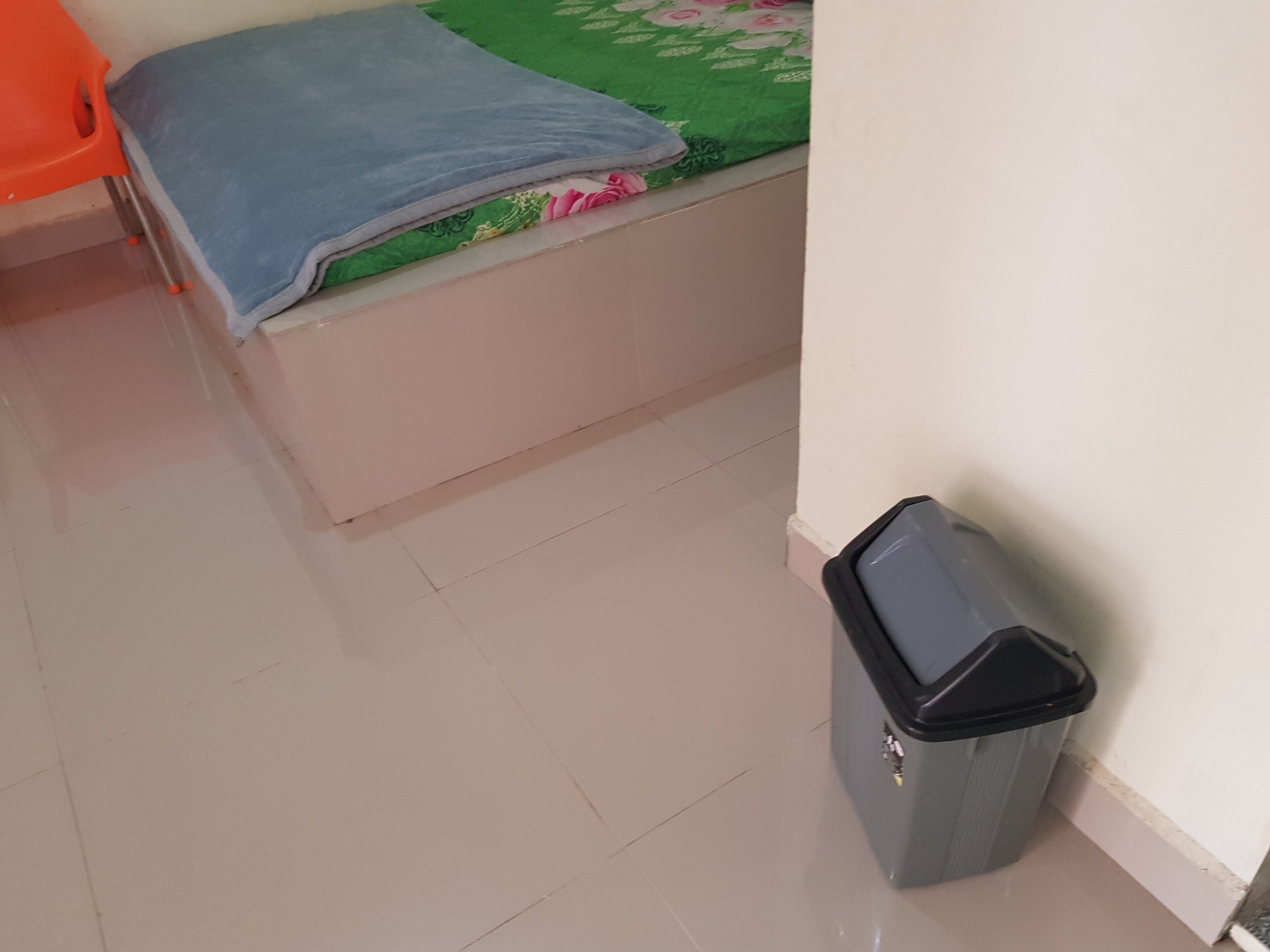 Una habitación pequeña con una cama, un cubo de basura y una pared.