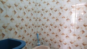 Un baño con inodoro, un cubo de basura azul y una escoba apoyada en la pared.