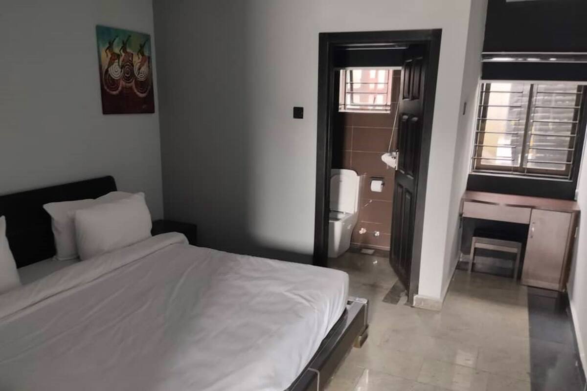 A bedroom with a bed, a desk, and a bathroom.