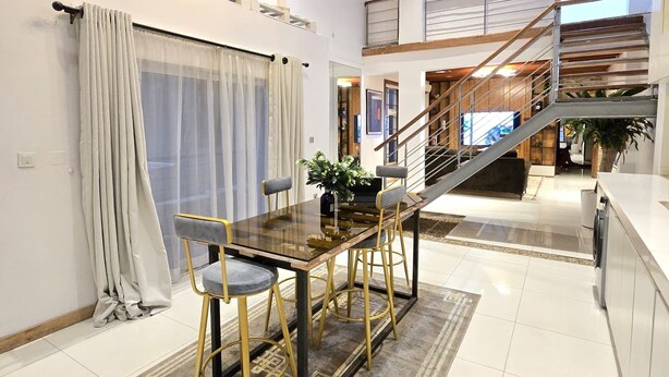 Un vaste espace dédié à la salle à manger, avec une table et des chaises en bois, un escalier et une vue sur l’extérieur.