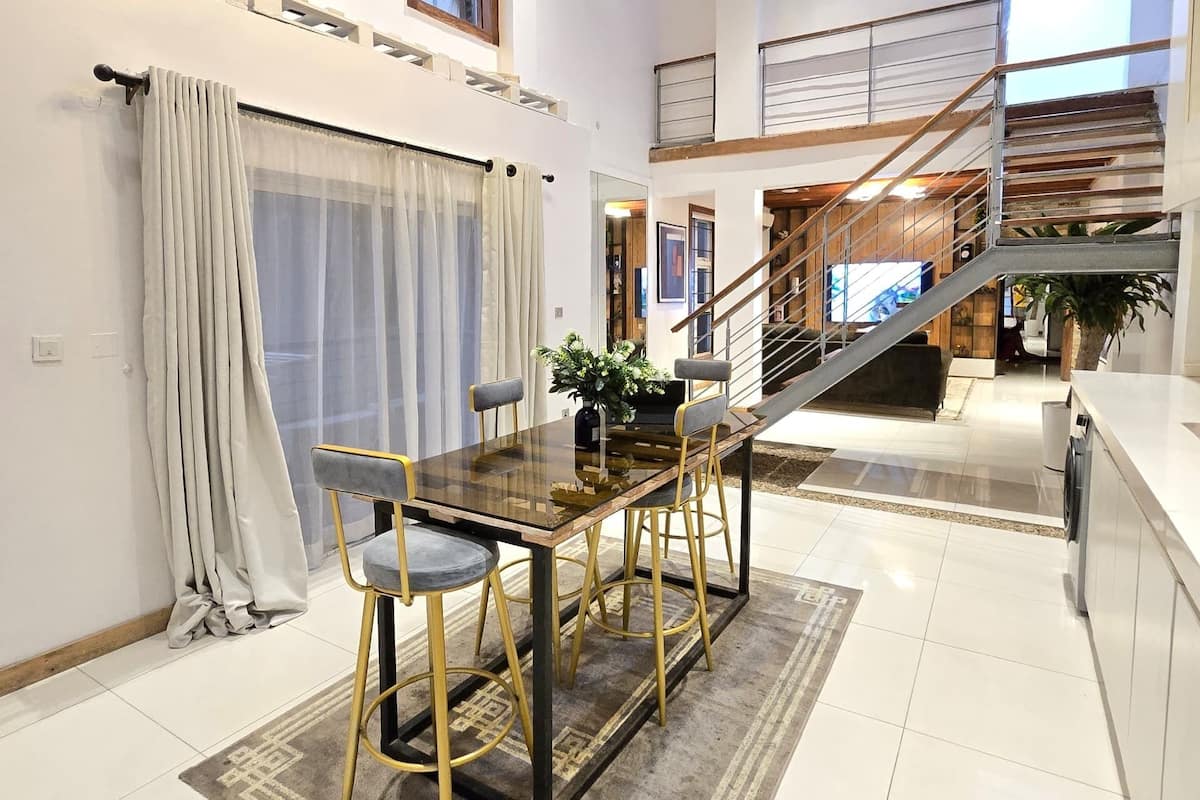 A spacious dining area with a wooden table and chairs, a staircase, and a view of the outdoors.