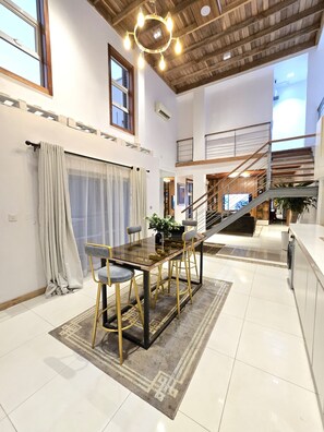 A spacious dining area with a wooden table and chairs, a staircase, and a view of the outdoors. - Home away from home  (Lekki)