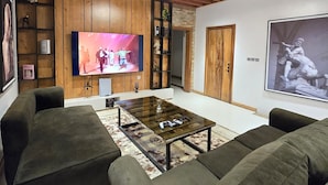 Un salon moderne avec des poutres apparentes en bois au plafond, un téléviseur à écran plat, deux canapés, une table basse et un grand tableau.