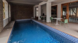 Une piscine dont le bord est revêtu de carrelage, entourée d’un patio couvert aménagé avec des tables et des chaises.
