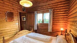 Une chambre de style cabane en bois avec deux lits, une fenêtre avec des rideaux, un radiateur fixé au mur et une petite table avec une lampe.