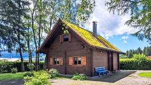 Une cabane en bois avec un toit en pente, une cheminée et un banc à l’extérieur.