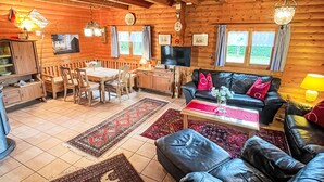 L’intérieur d’un chalet confortable, avec une salle à manger, un salon doté d’un canapé et d’une table basse, et un téléviseur placé dans un coin.