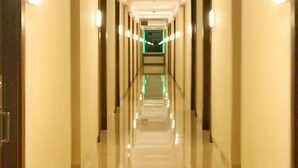 A long, well-lit hallway with doors on both sides, leading to a green-lit room at the end. - Collection O 93707 Rooms By U (Berastagi)