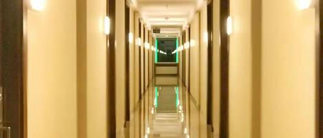 A long, well-lit hallway with doors on both sides, leading to a green-lit room at the end.