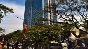 A tall, modern skyscraper with a glass facade, surrounded by trees and urban elements. - Collection O 93707 Rooms By U (Berastagi)