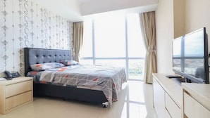 A modern bedroom with a large bed, a bedside table with a phone, a TV on a stand, and a view of the city through large windows. - Collection O 93707 Rooms By U (Berastagi)