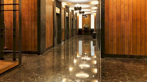 A hallway with wooden paneling and a polished marble floor, leading to a reception area with a plant and a desk. - Collection O 93707 Rooms By U (Berastagi)
