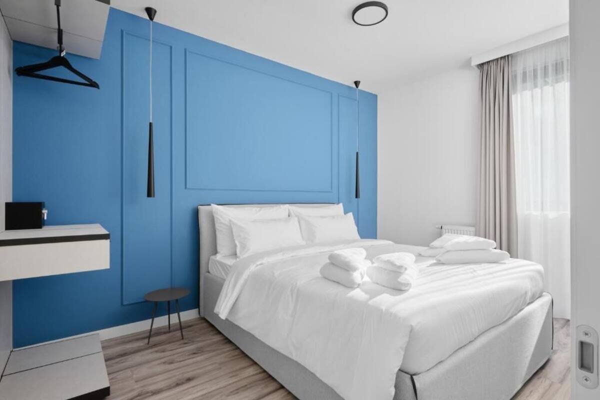 Una habitación de hotel moderna con una pared azul de acento, una cama bien hecha con ropa de cama blanca, una mesita de noche pequeña y una lámpara colgante.