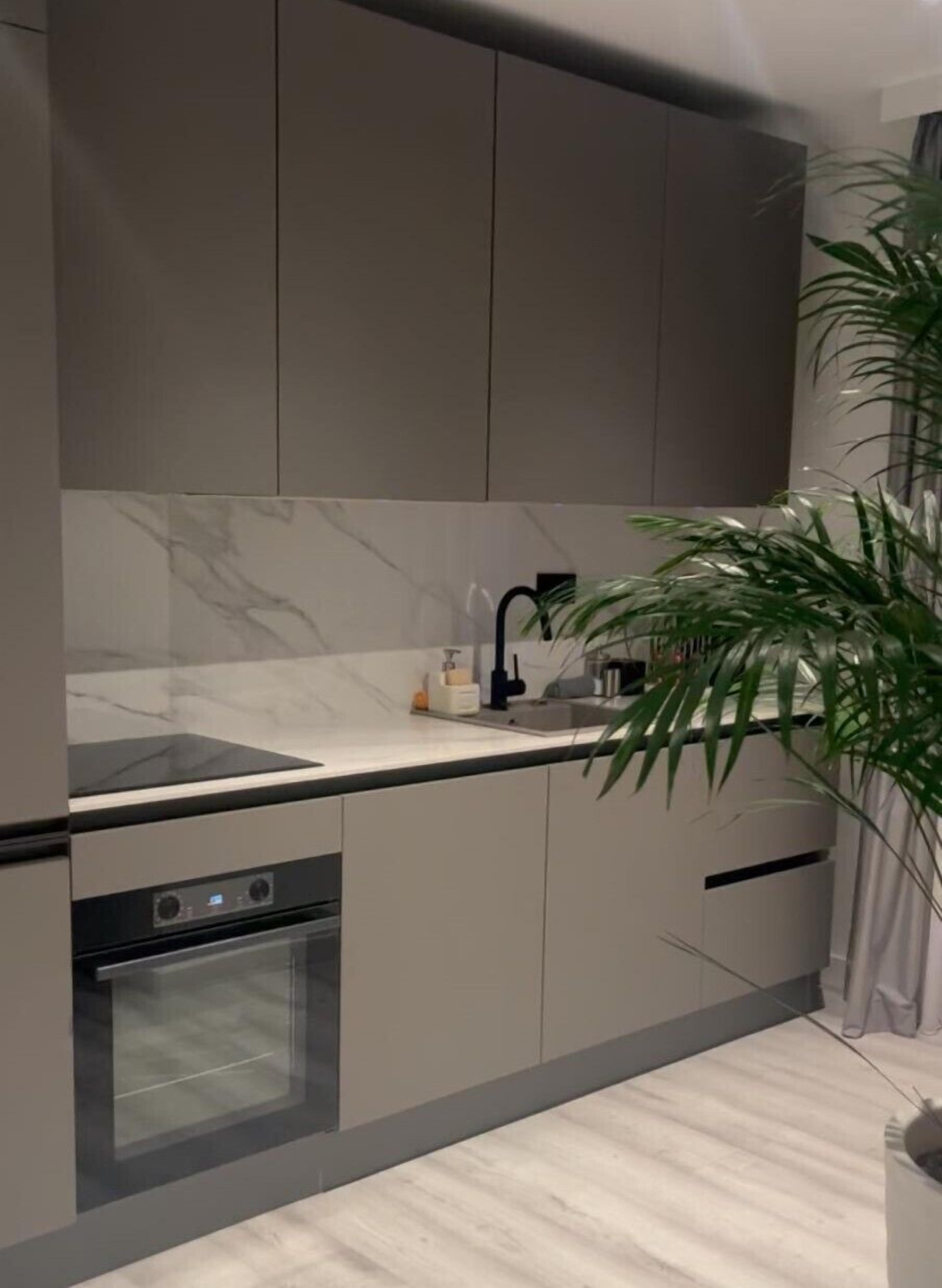 Een moderne keuken met grijze kastjes, een marmeren spatwand, een ingebouwde oven en een gootsteen met een zwarte kraan.
