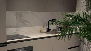 Een moderne keuken met grijze kastjes, een marmeren spatwand, een ingebouwde oven en een gootsteen met een zwarte kraan.
