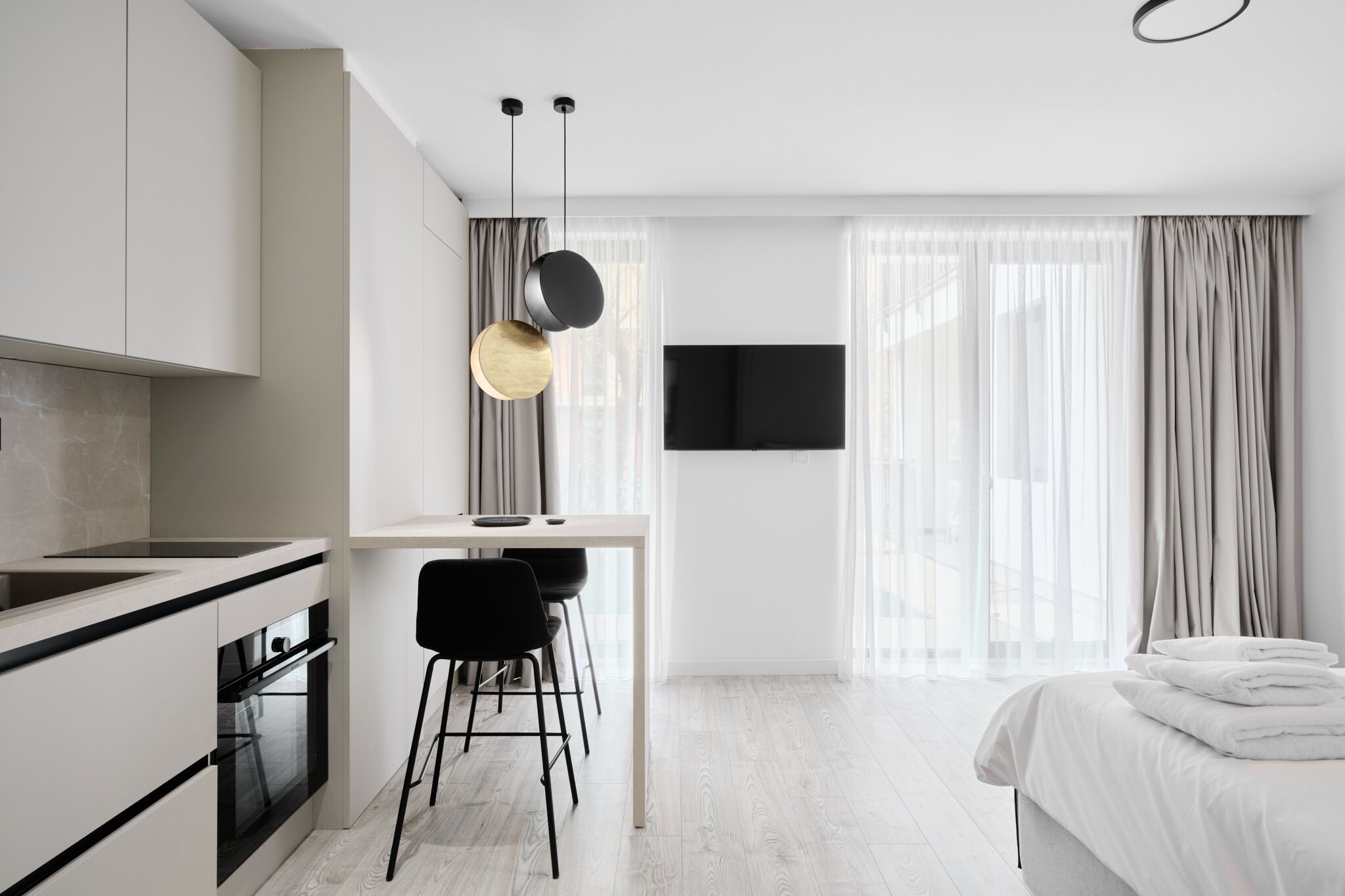 Una habitación de hotel moderna con kitchenette, zona de comedor y cama con toallas ordenadas.