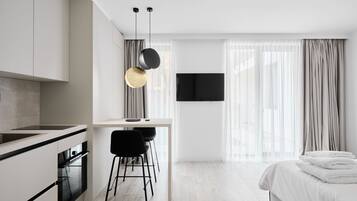 Una habitación de hotel moderna con kitchenette, zona de comedor y cama con toallas ordenadas.