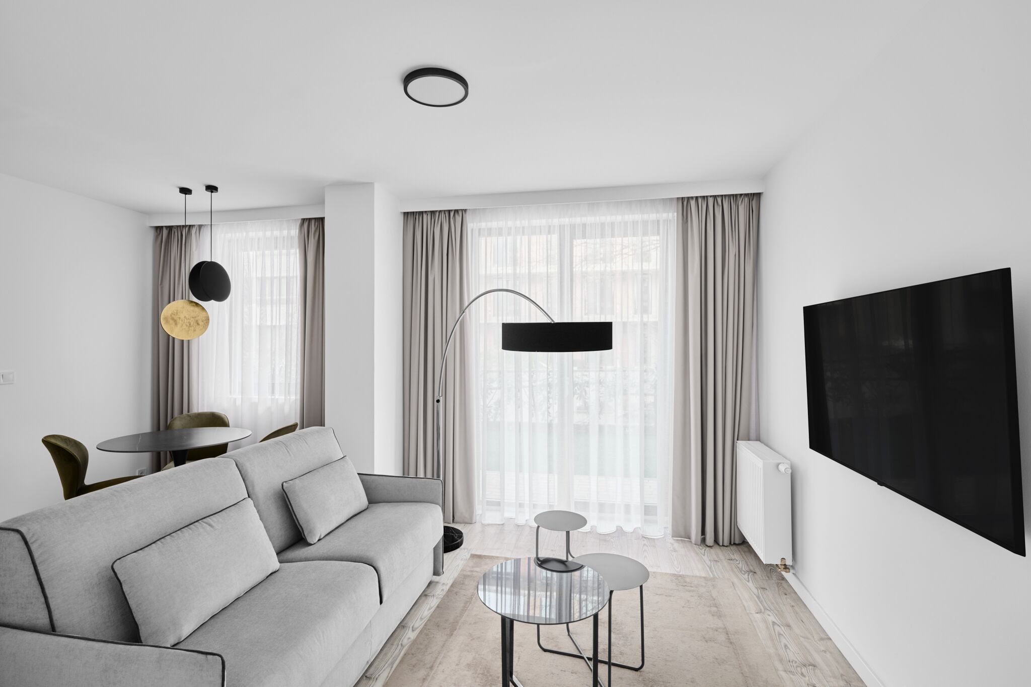 Una sala de estar moderna con un sofá gris, una mesa redonda, un televisor y un comedor con mesa y sillas.