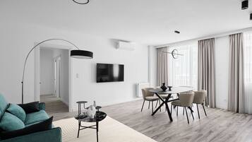 Een moderne woonkamer met een bank, salontafel, televisie en een eethoek met stoelen en een tafel.