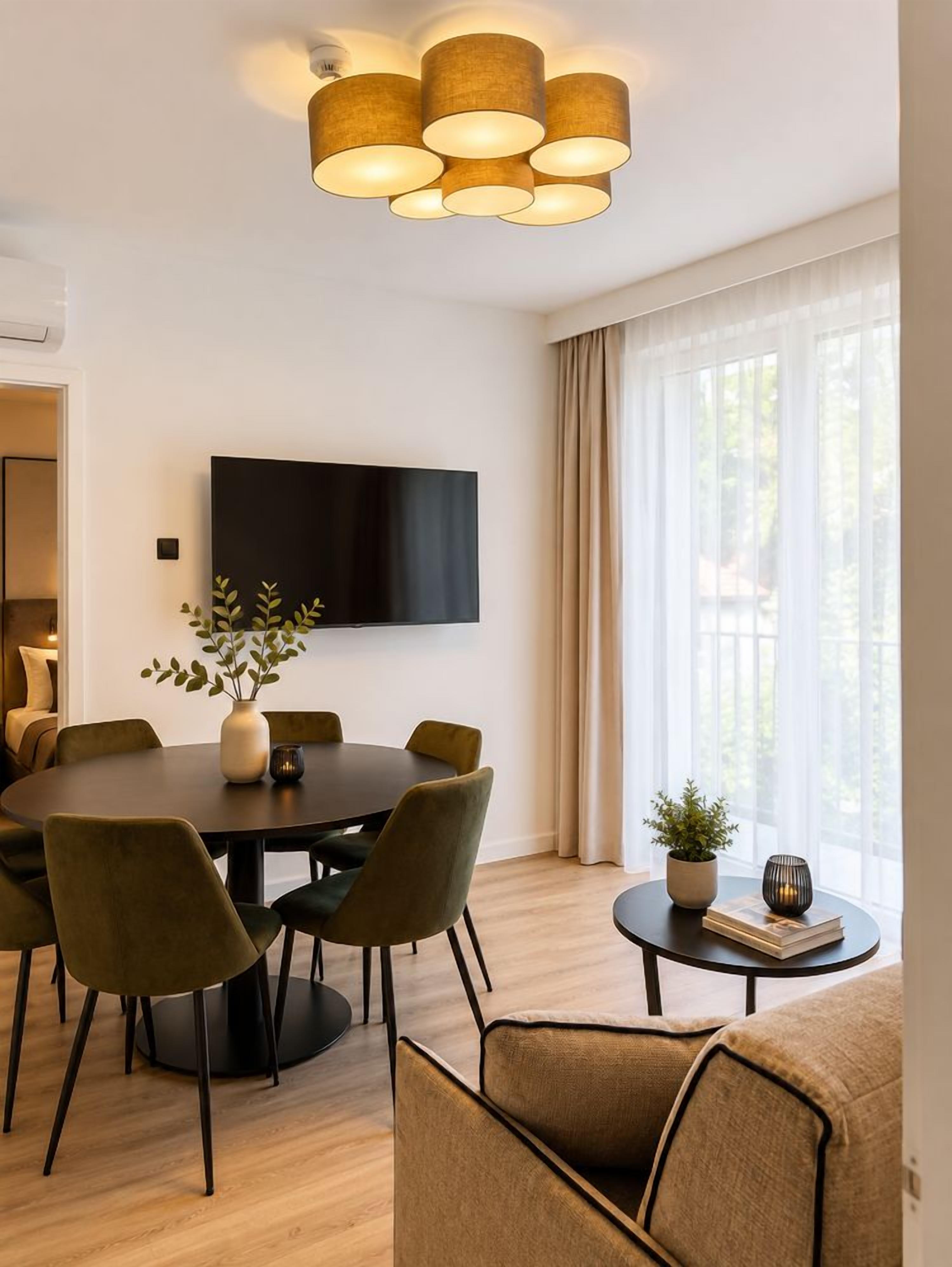 Un comedor moderno con una mesa redonda, sillas, un televisor de pantalla plana en la pared y un amplio ventanal con cortinas.