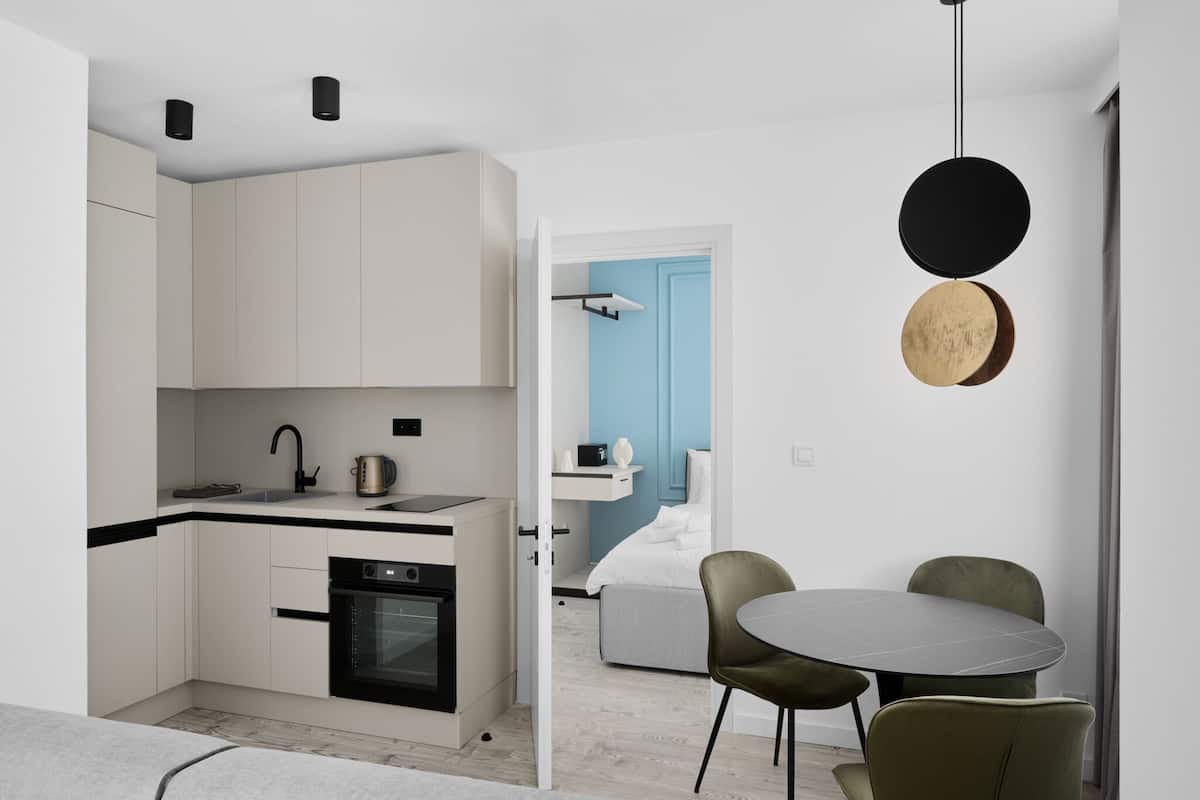 Cocina moderna con armarios blancos, encimera negra y horno integrado. Cuenta con una zona de comedor con una mesa redonda y dos sillas.