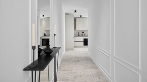 Un pasillo estrecho con una mesa negra y candelabros, que conduce a una cocina moderna con armarios blancos y una encimera de mármol.