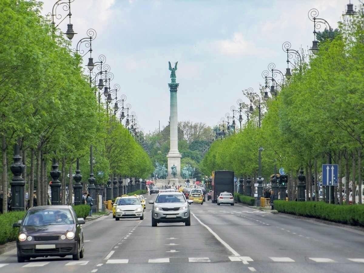 A wide road with a central monument, flanked by trees and street lamps.