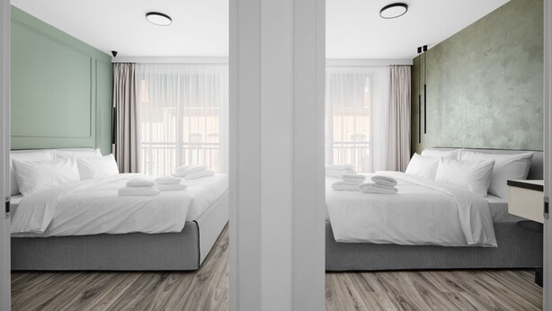 Una habitación de hotel moderna con cama, mesitas de noche y un amplio ventanal con cortinas.