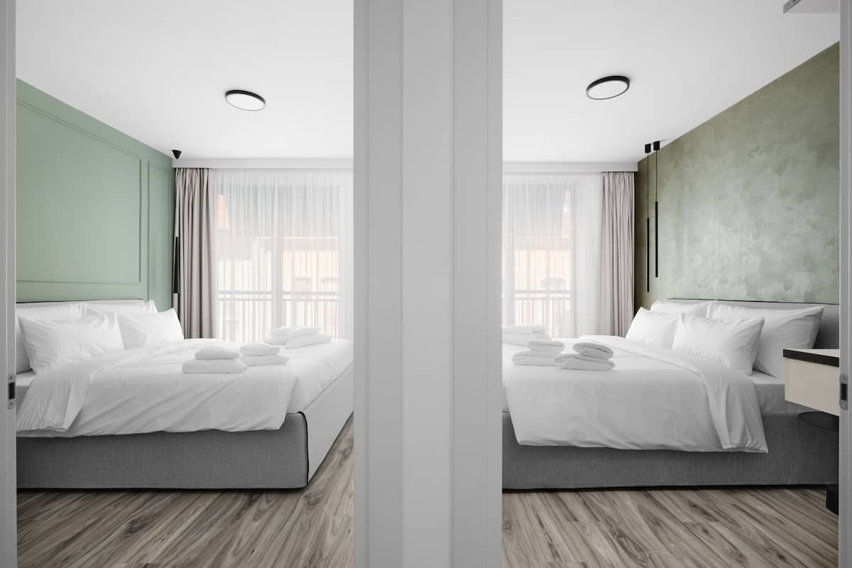 Una habitación de hotel moderna con cama, mesitas de noche y un amplio ventanal con cortinas.