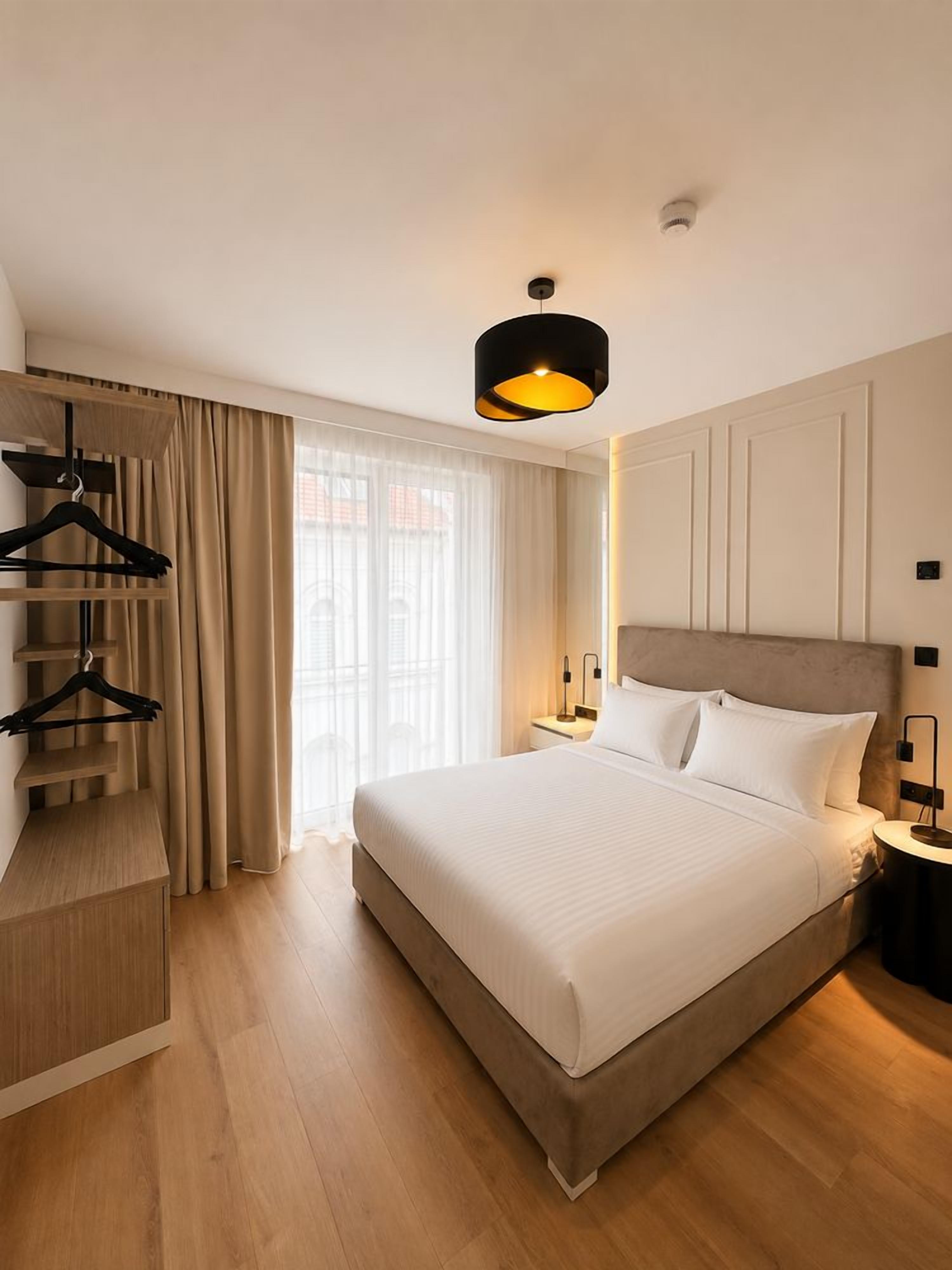 A hotel room with a large bed, a wardrobe, a bedside table, and a hanging light fixture.