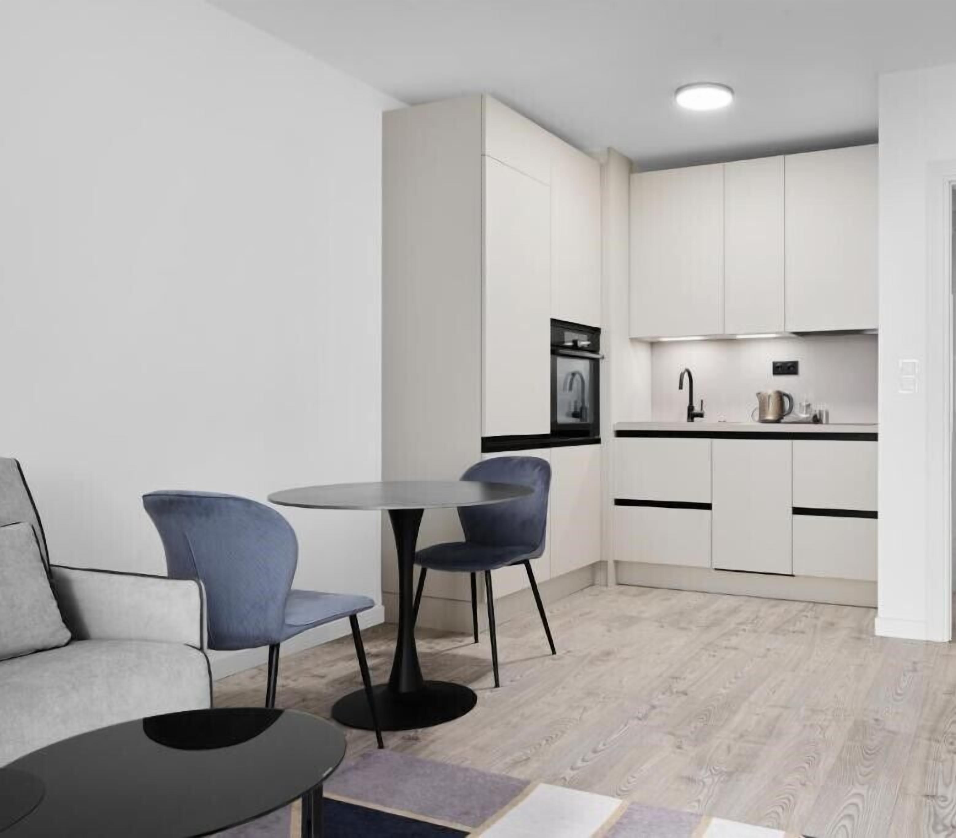En moderne, kompakt opholdsstue med spiseplads, tekøkken og siddeområde med sofa og stole.