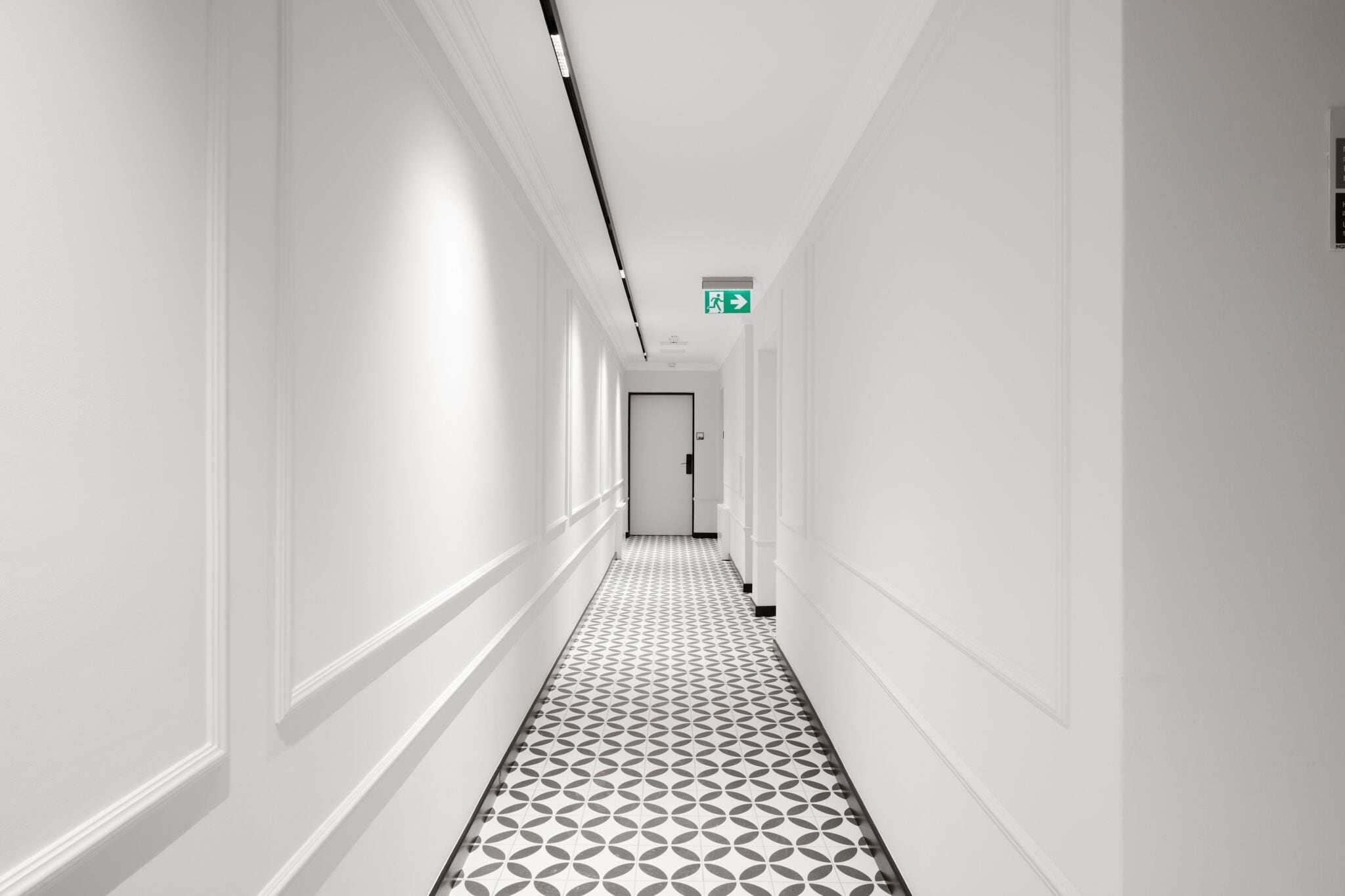 A long, narrow hallway with white walls and a patterned floor, leading to a door at the end.