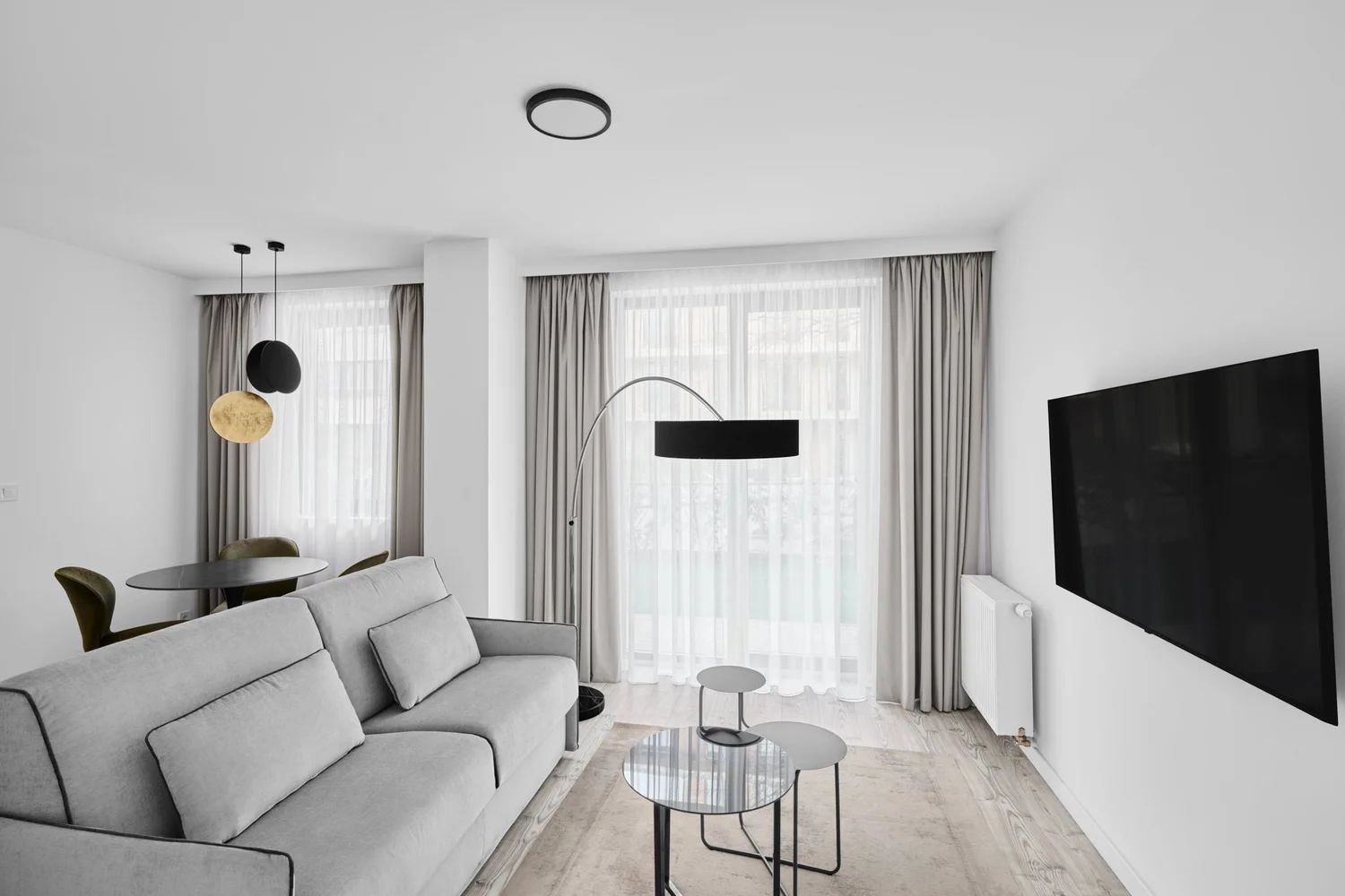 Una sala de estar moderna con un sofá, una mesita redonda, una lámpara de pie y un televisor de pantalla plana montado en la pared.