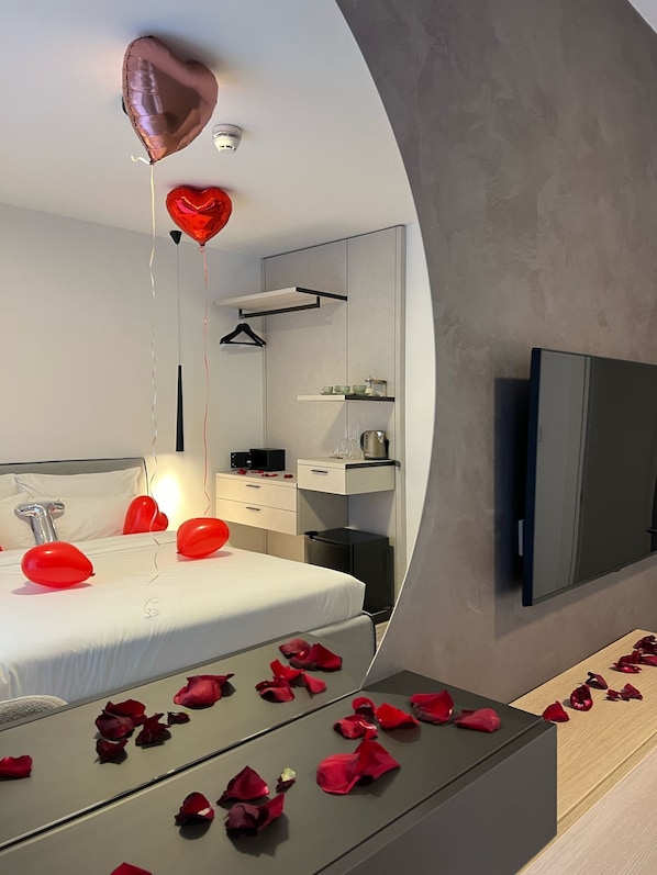 A modern bedroom with a bed, bedside tables, a mirror, a TV, and a floating heart-shaped balloon.