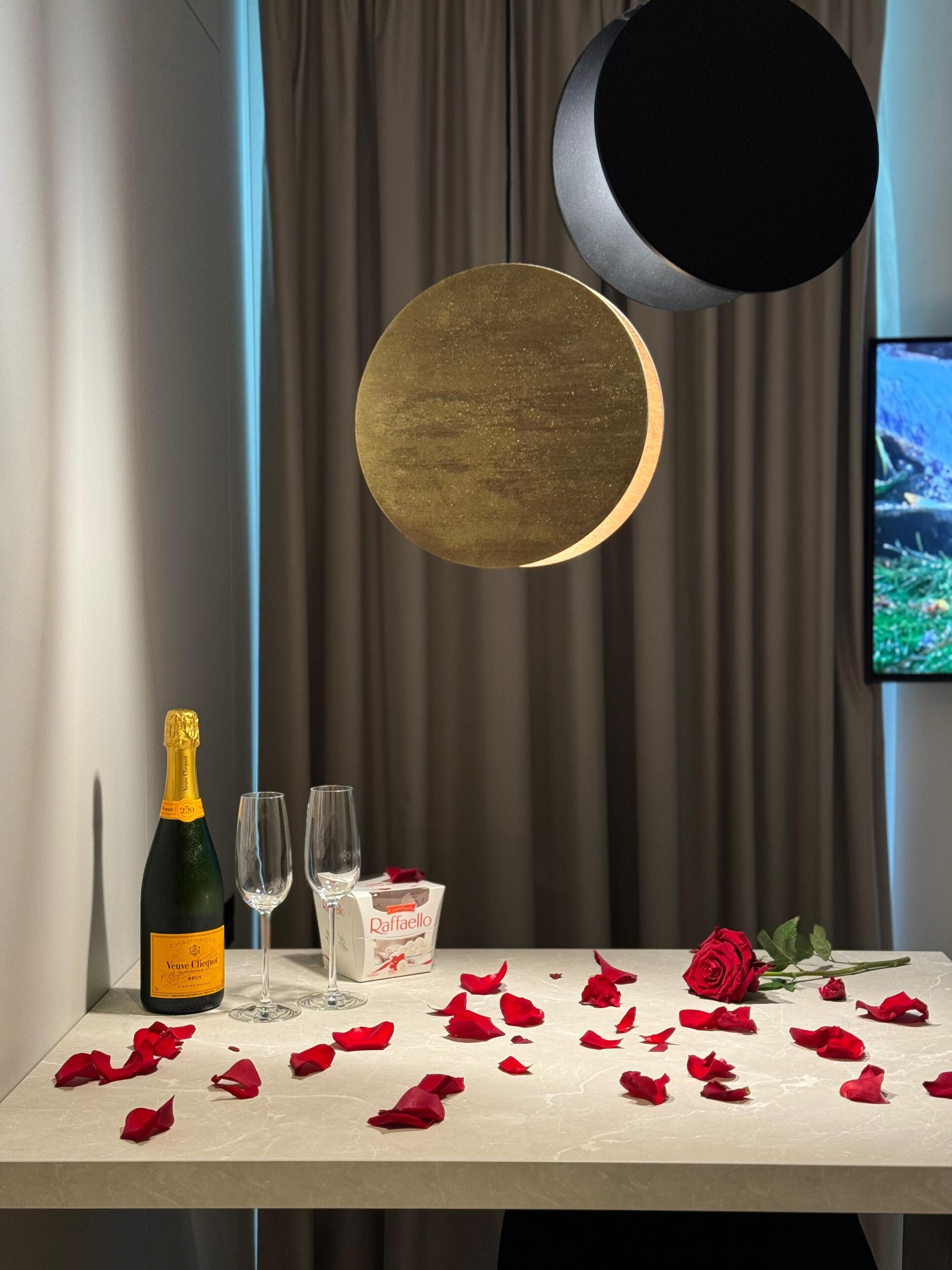Ein Tisch mit einer Champagnerflasche, zwei Gläsern, einer Raffaello-Schachtel und verstreuten Rosenblättern.