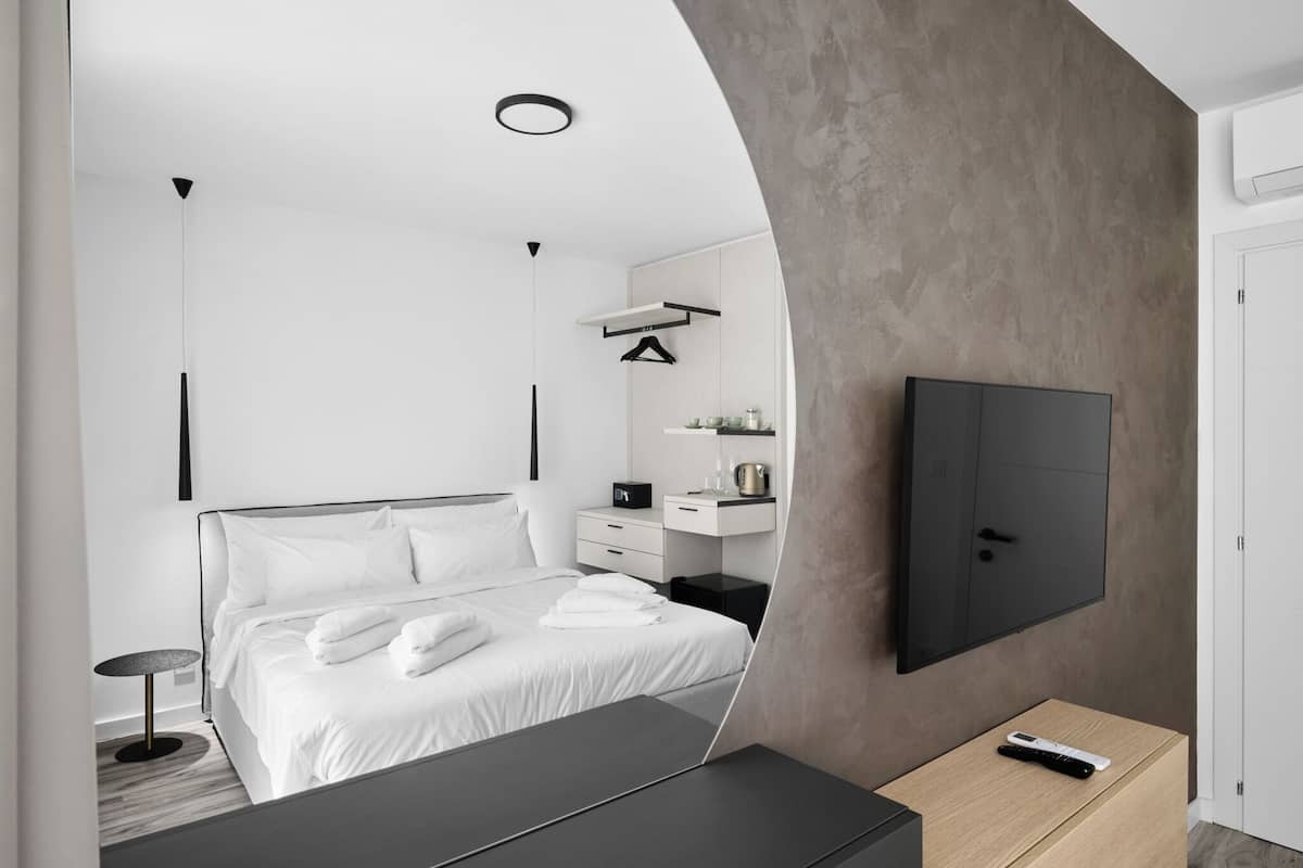Una habitación de hotel moderna con una cama grande, una mesita de noche, un televisor montado en la pared y un pequeño escritorio con una silla.