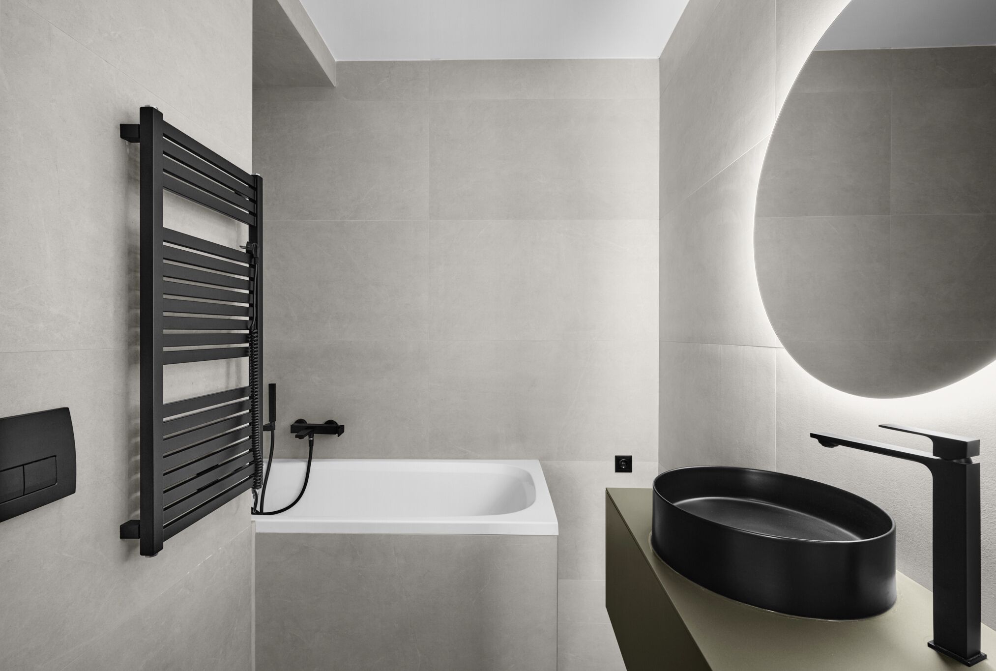 A modern bathroom with a freestanding bathtub, a black towel rack, a round black sink, and a large mirror.