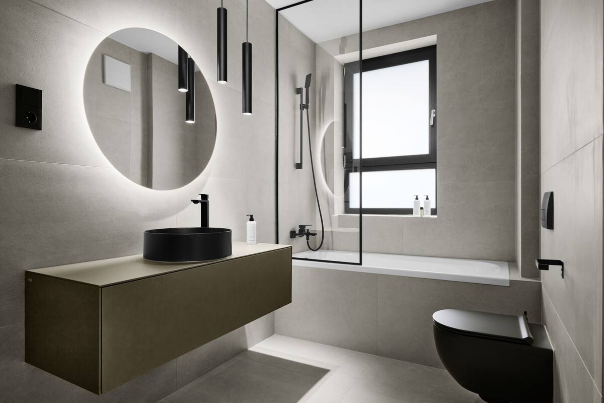 Un baño moderno con un espejo redondo, un lavamanos negro, inodoro y ducha.