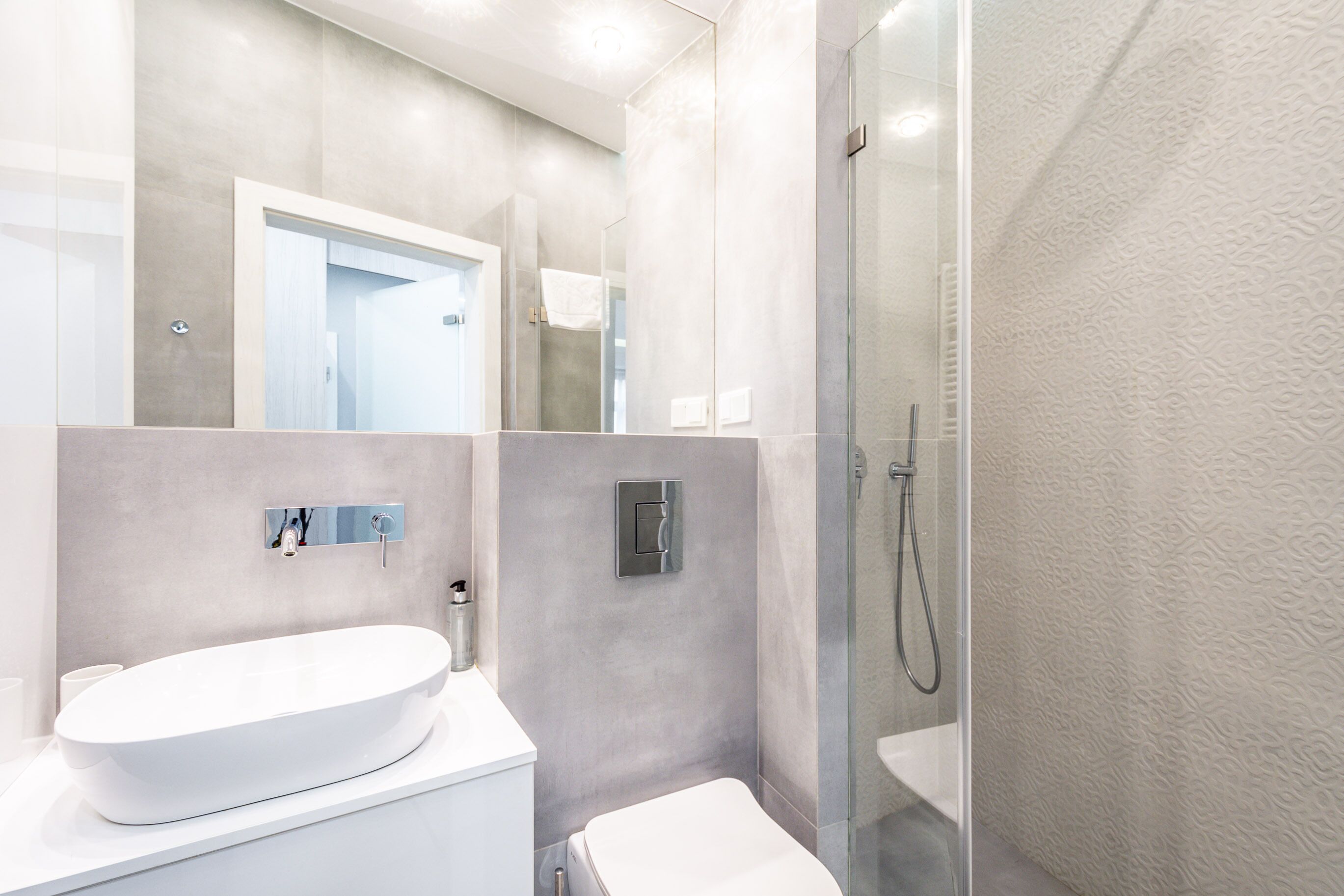 A modern bathroom with a large white sink, a glass-enclosed shower, and a toilet.