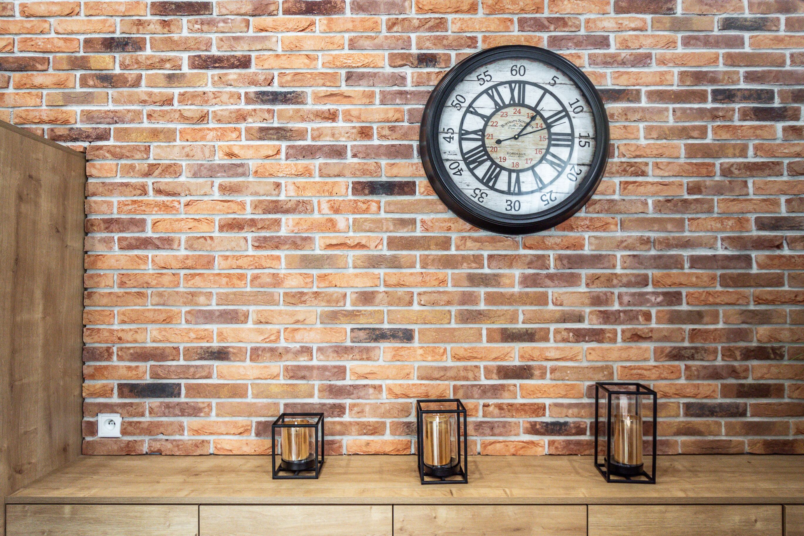 A brick wall with a round clock and three candle holders.